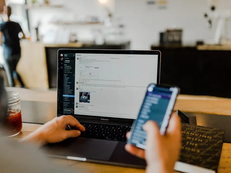 Persona trabajando con un portátil y un teléfono móvil a la vez en una cafetería