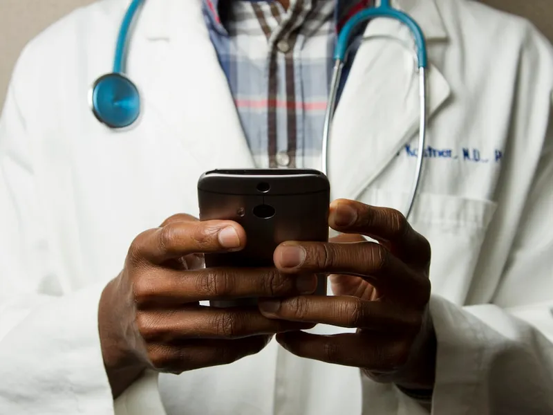 Profesional sanitario con bata blanca y estetoscopio consultando un teléfono móvil